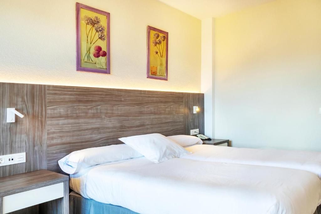 A double bed with white bedding, a wooden headboard, and two wall-mounted nightstands with lamps.