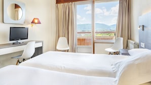 A hotel room with a bed, a desk with a computer, a chair, a TV, and a balcony with curtains. - Hotel Vejo (Reinosa)