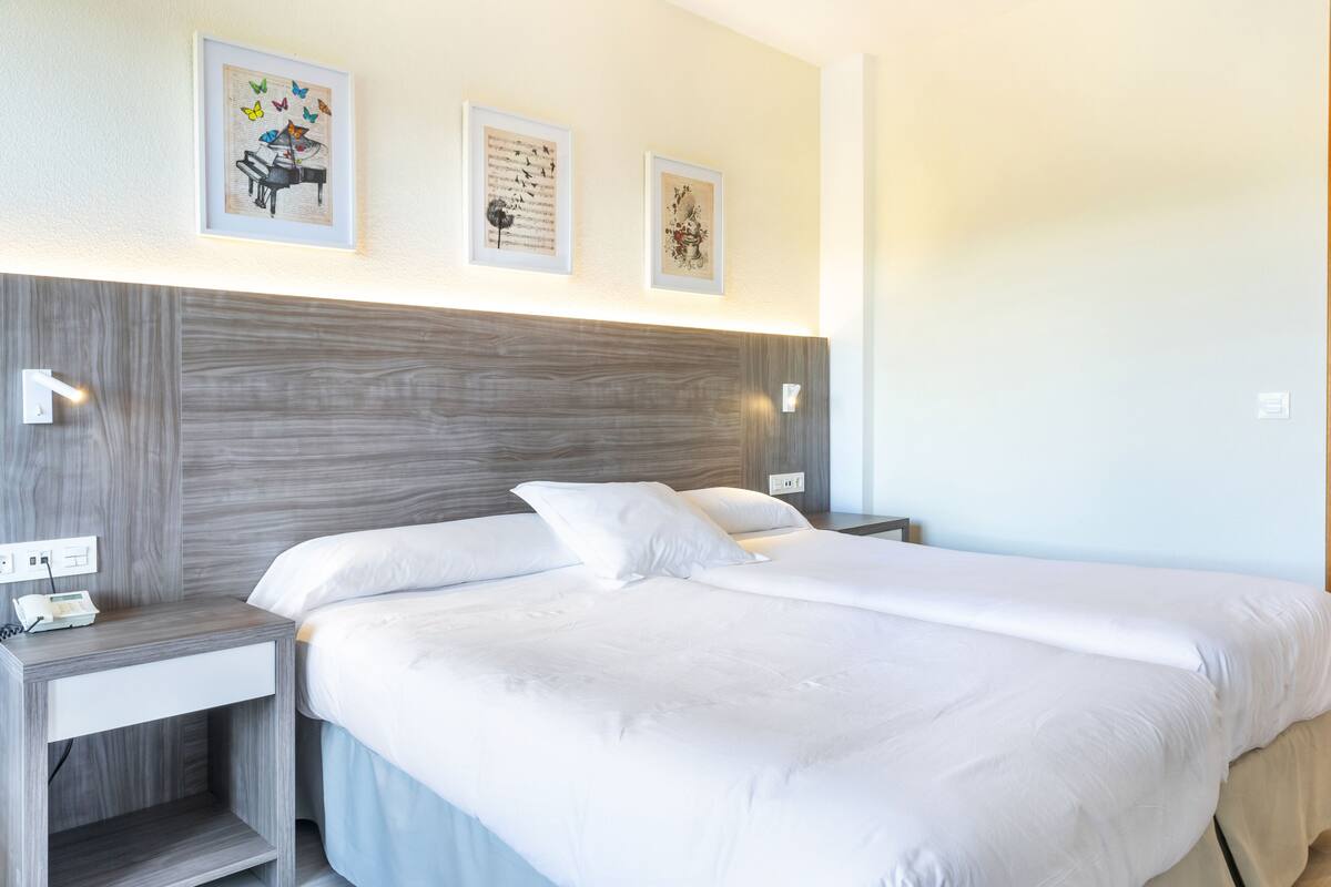 A hotel room with a large bed, a bedside table with a lamp, and three framed artworks on the wall.
