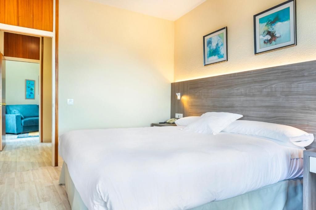 Habitación de hotel con cama, mesita de noche, luz de pared y puerta que da a otra habitación.