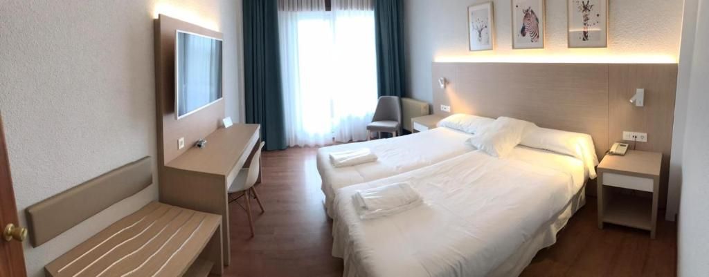 Habitación de hotel con dos camas, un escritorio, una silla y un televisor.