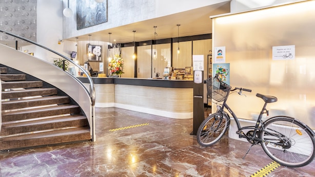 A hotel lobby with a curved staircase, a reception desk, and a bicycle parked by the wall. - Hotel Vejo (Reinosa)