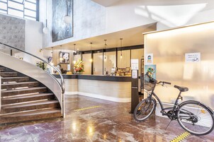 Um saguão de hotel com uma escadaria curva, um balcão de recepção e uma bicicleta encostada na parede.
