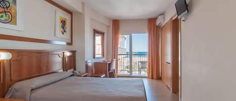 A hotel room with a large bed, a desk, a chair, a TV, and a balcony with a view.