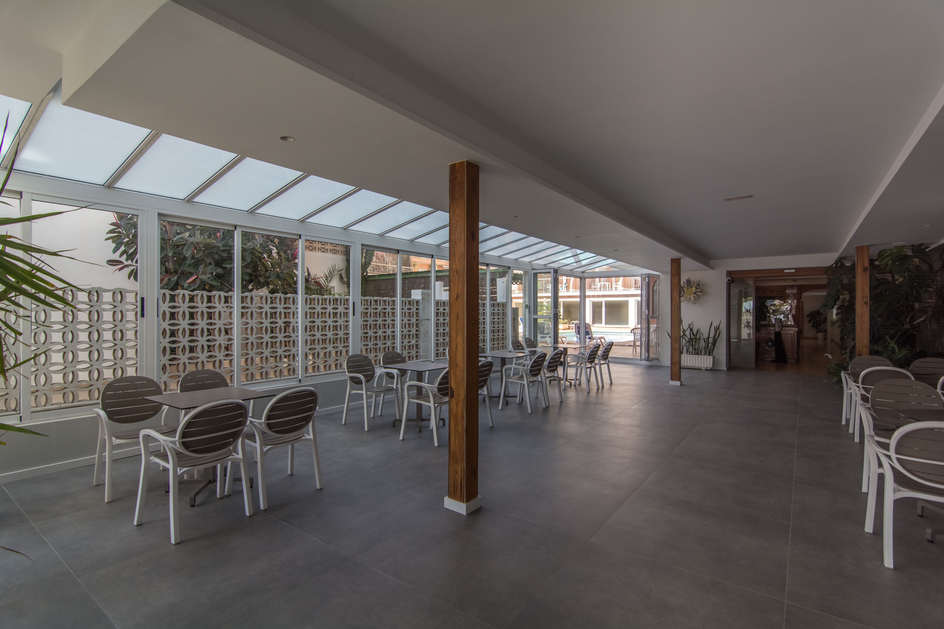Un espacio interior amplio con techo alto, ventanas grandes y una zona de estar con mesas y sillas.