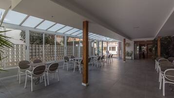 Un espacio interior amplio con techo alto, ventanas grandes y una zona de estar con mesas y sillas.