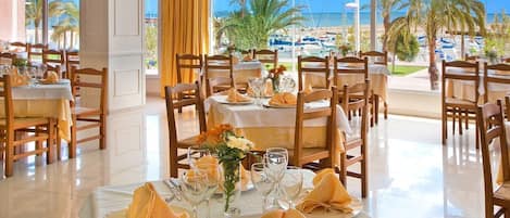 A restaurant with multiple tables set for dining, featuring a view of the sea and boats.