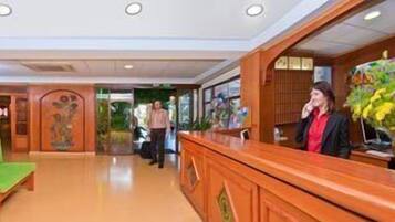 Un hall de hotel con una recepción, un sofá verde y una planta decorativa.