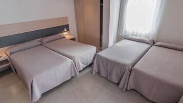 A hotel room with two single beds, a nightstand, a wardrobe, and a window with curtains.