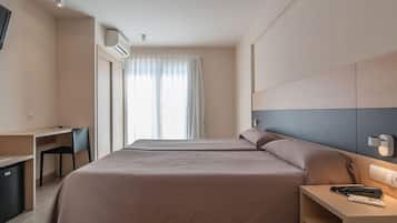 A modern hotel room with a large bed, a desk, and a chair. There is an air conditioning unit on the wall and a window with curtains.