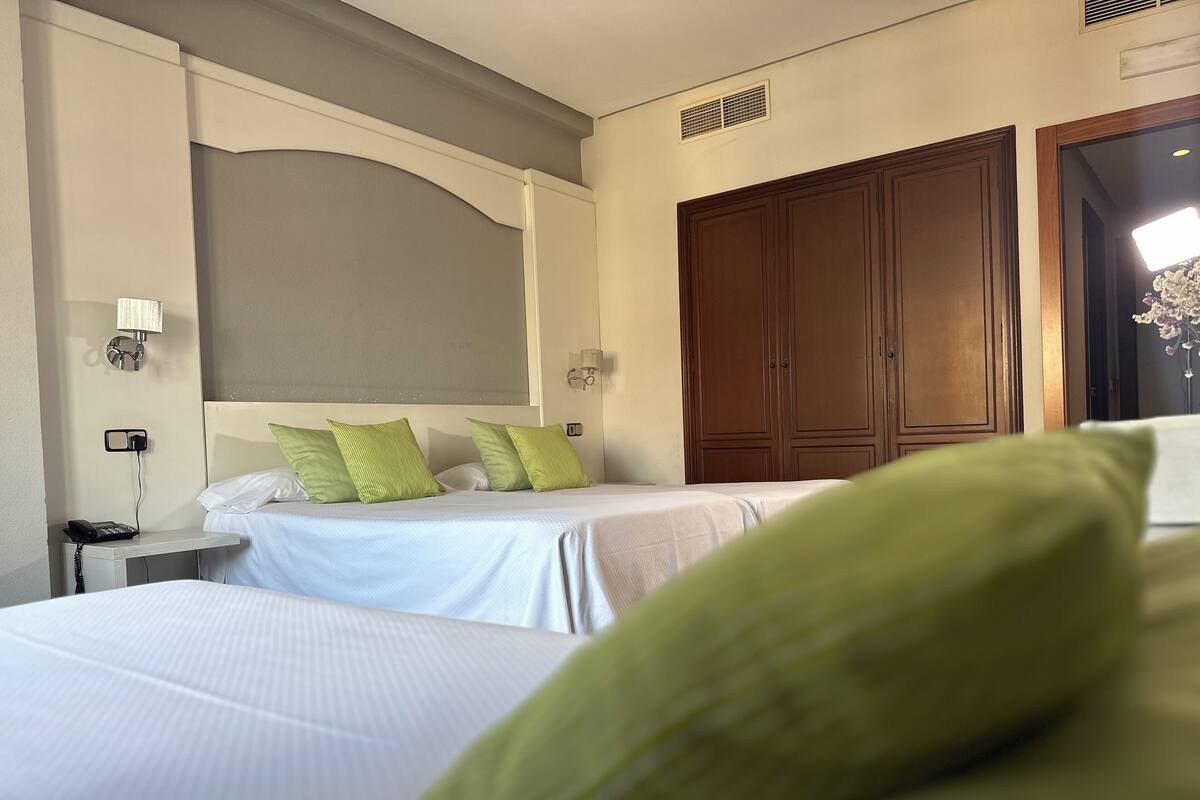 Una habitación de hotel con dos camas, una mesita de noche, un teléfono y un armario grande.