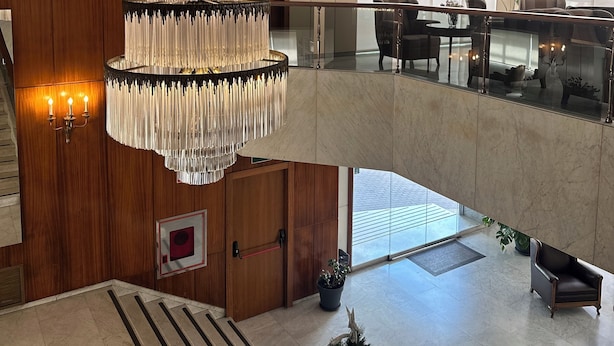 A multi-level hotel lobby with a large chandelier, wooden paneling, a reception desk, and a seating area with a view of the city. - Hotel Mir Octavio (Algeciras)