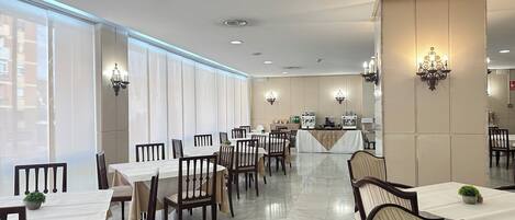 A hotel dining area with tables and chairs, a buffet station, and large windows.
