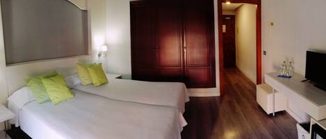 A hotel room with a bed, bedside table with a phone, a desk with a TV, and a wardrobe.