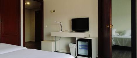 A hotel room with a bed, a desk with a computer and a television, and a small refrigerator.