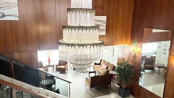 Un hall d’entrée spacieux, agrémenté d’un grand lustre décoratif, de boiseries, de sièges confortables et d’un escalier.