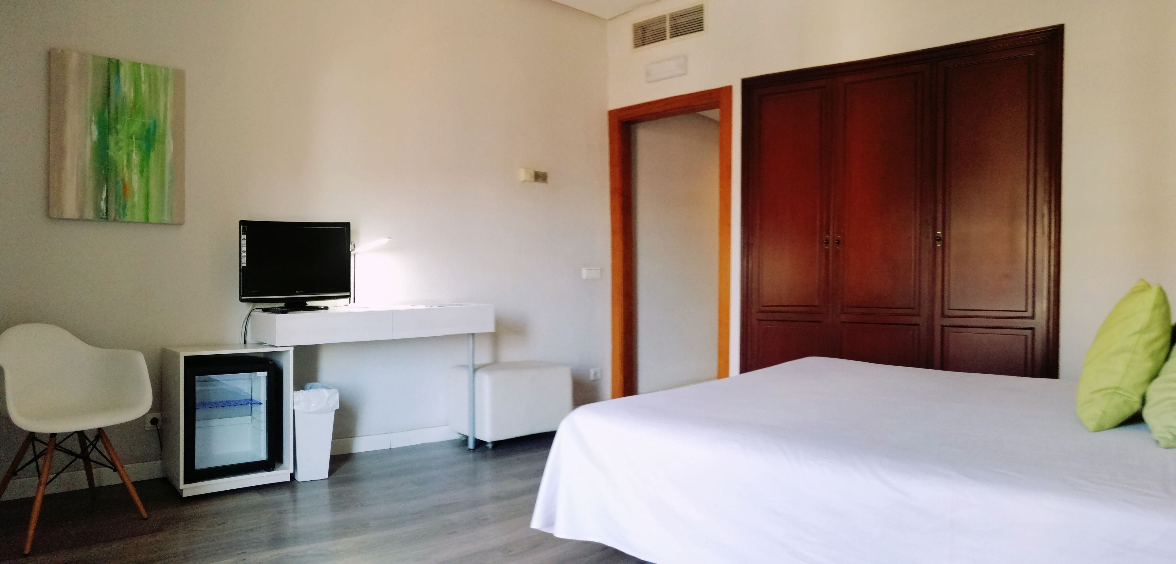 Una habitación de hotel con una cama, un escritorio con computadora, una silla y un armario.
