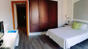Una habitación de hotel con cama, escritorio con televisor, armario y mesita de noche con lámpara.