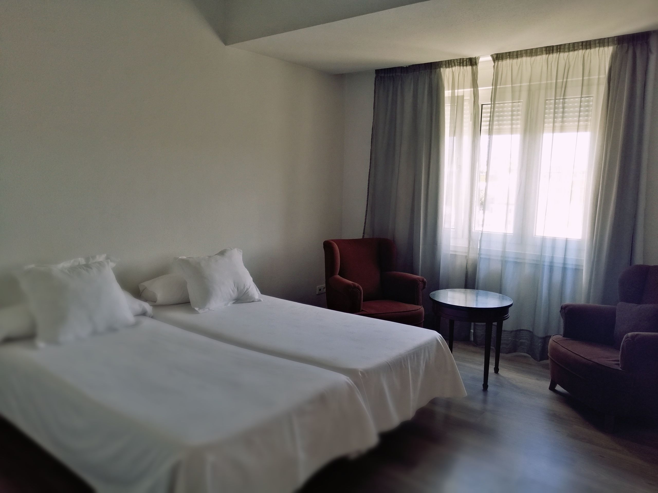 Une chambre d’hôtel avec deux lits, un fauteuil rouge, une petite table ronde et un canapé violet.