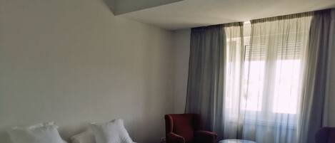 Une chambre d’hôtel avec deux lits, un fauteuil rouge, une petite table ronde et un canapé violet.