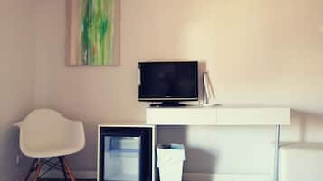 Una habitación moderna con un escritorio blanco, un televisor de pantalla plana, una silla blanca y un refrigerador pequeño.