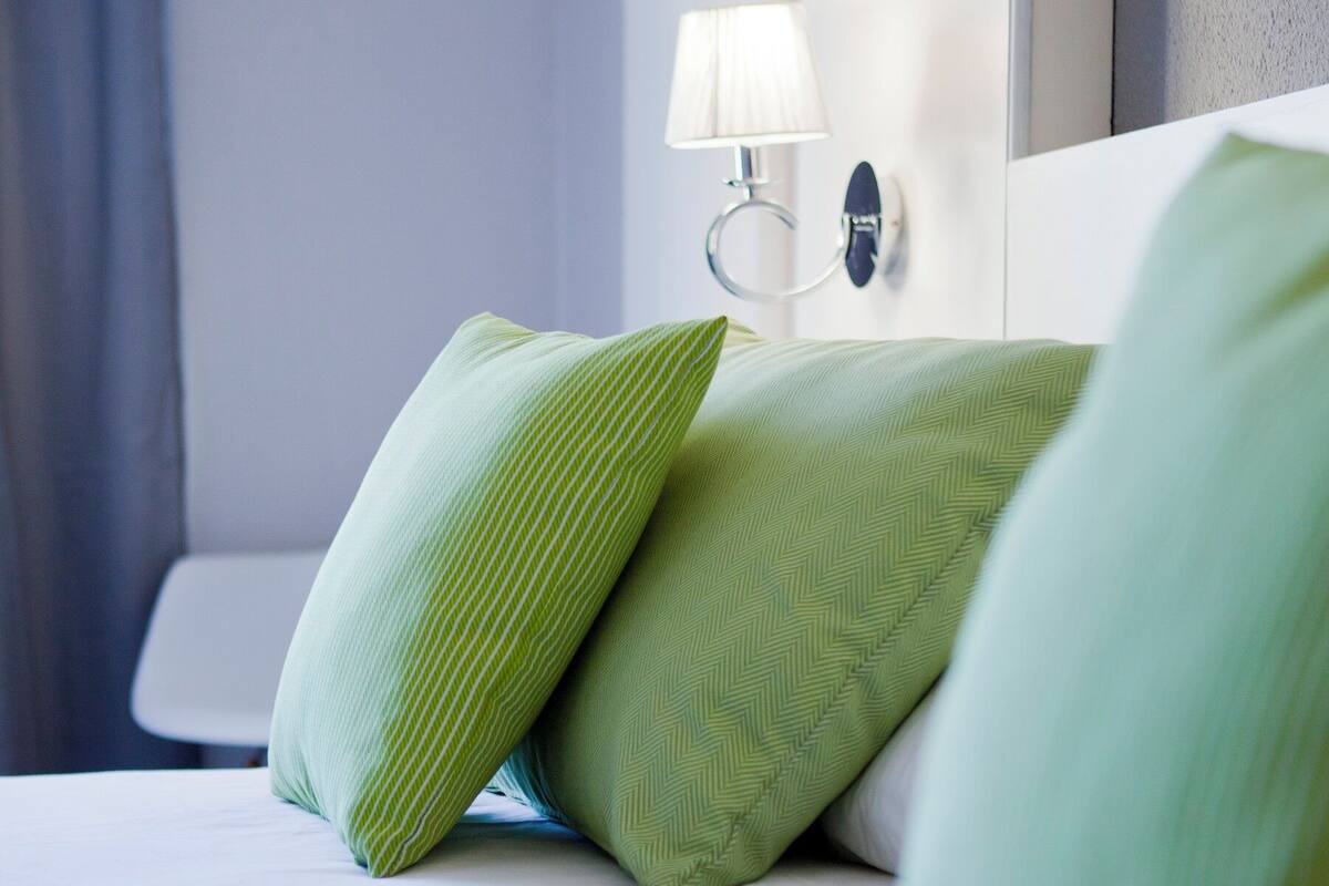 Una cama bien hecha con almohadas verdes y una lámpara de noche.