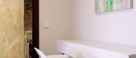 Un baño moderno con un tocador blanco, una silla blanca y un cuadro abstracto verde en la pared.