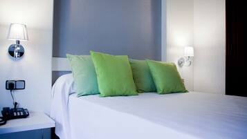 Una cama bien hecha con almohadas verdes, una lámpara de noche y un teléfono en la mesita de noche.