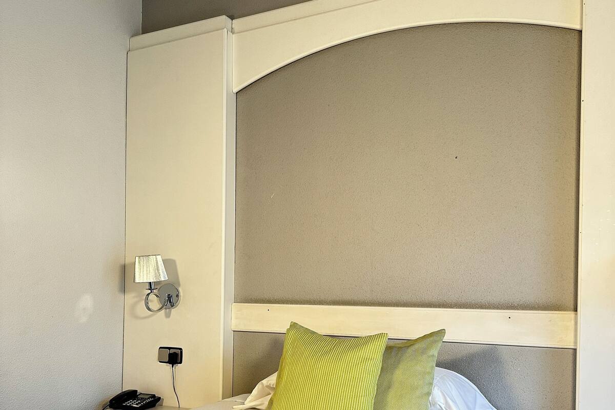 Habitación de hotel con una cama grande, teléfono en la mesita de noche, lámpara y luz empotrada en la pared.