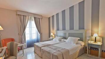 Habitación de hotel con dos camas, un escritorio, una silla y un ventanal con cortinas.