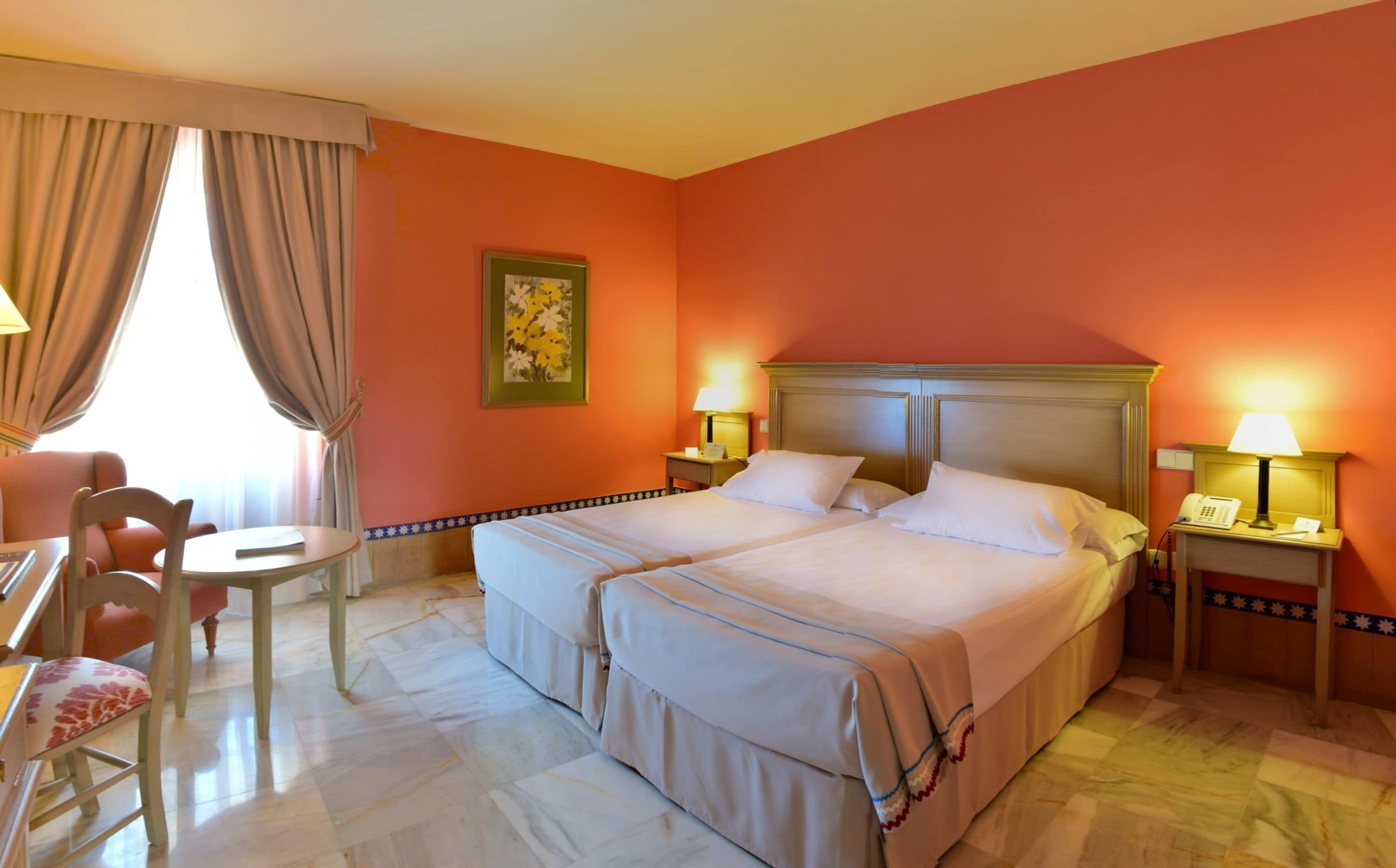 A hotel room with a large bed, two bedside tables with lamps, a desk with a chair, and a painting on the wall.