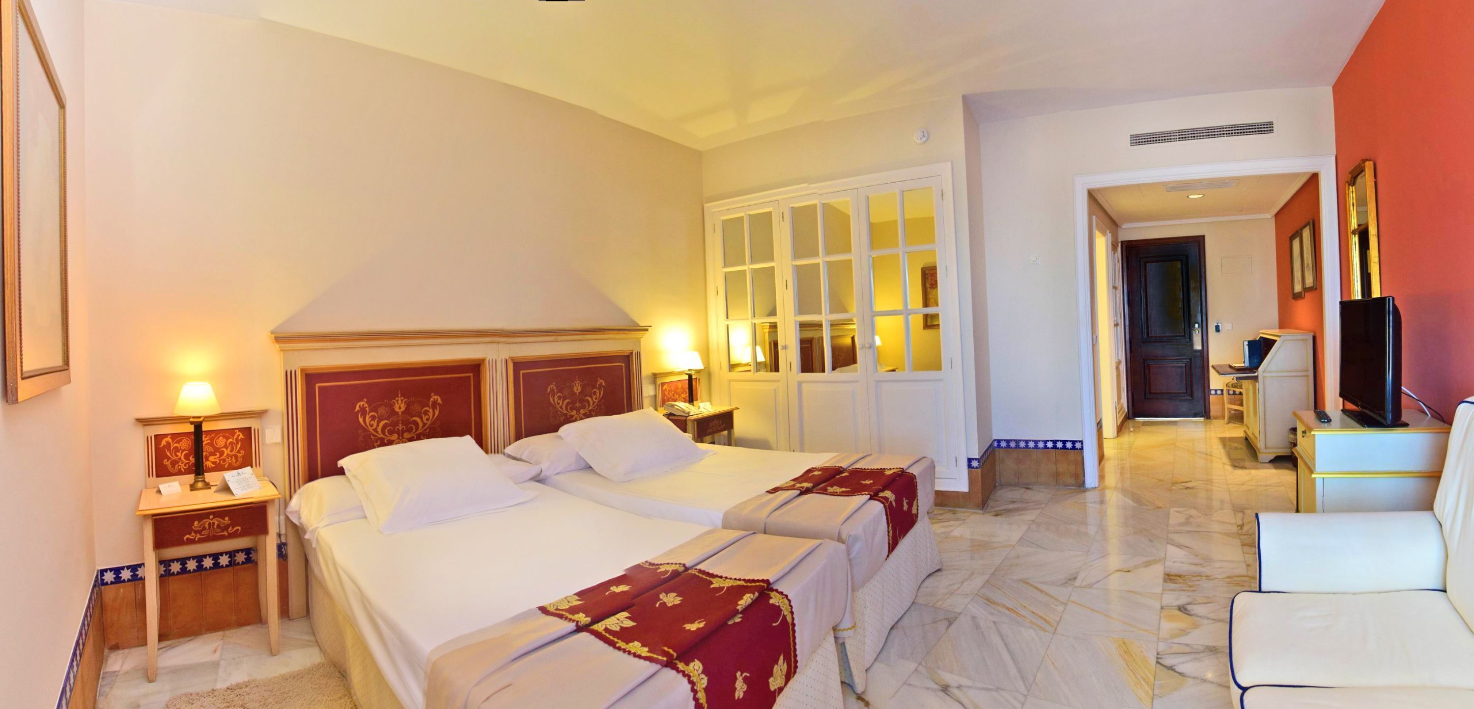 Habitación de hotel con dos camas, un escritorio, una silla, un televisor y un baño visible a través de una puerta abierta.