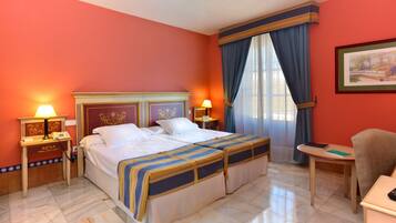 A hotel room with a double bed, two bedside tables with lamps, a chair, a small table, and a painting on the wall.