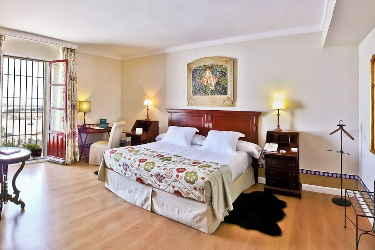 Una habitación de hotel con una cama grande, dos sillas, una mesita, un escritorio y una lámpara.