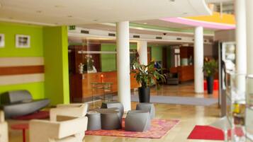 Un lobby moderno con una mesa de recepción, zona de estar y una planta grande en maceta.