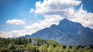 A mountain landscape with a prominent peak, dense forest in the foreground, and a clear sky with scattered clouds.