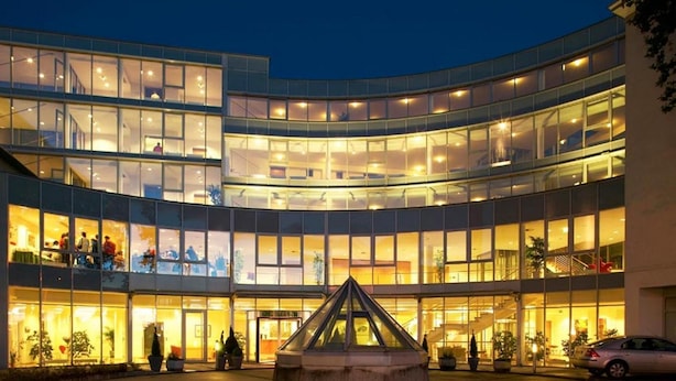 Un edificio moderno de varios pisos, amplios ventanales y un patio central con una escultura geométrica.