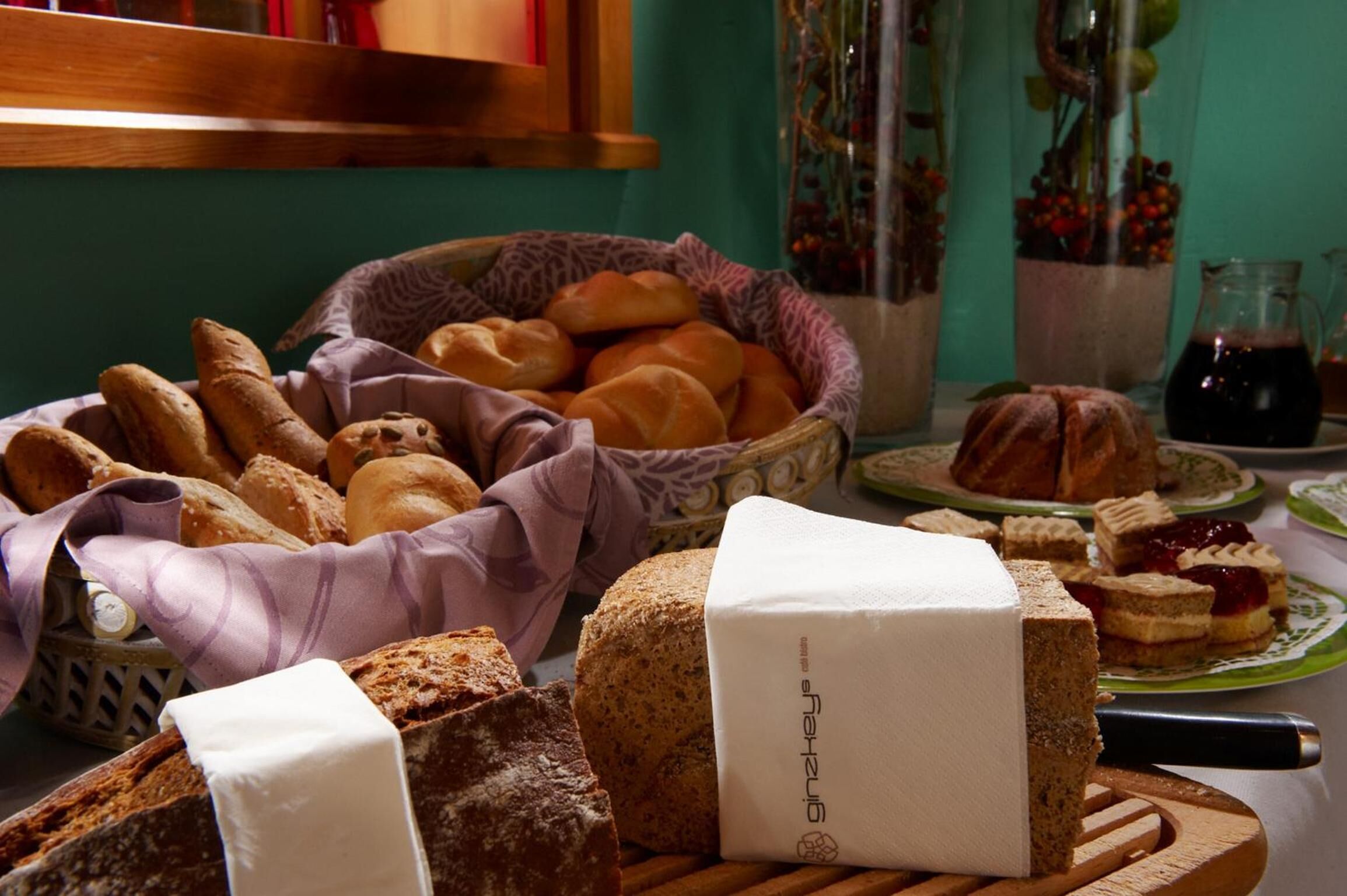 Diverse broden en gebak op een tafel, waaronder een brood met een etiket, een mandje met broodjes en een bord met belegde broodjes.