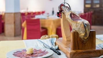 Un soporte de madera para cortar carne con un gran trozo de carne, un plato con carne en rodajas y un pequeño trozo de mantequilla, y un cuchillo sobre una mesa en un comedor.
