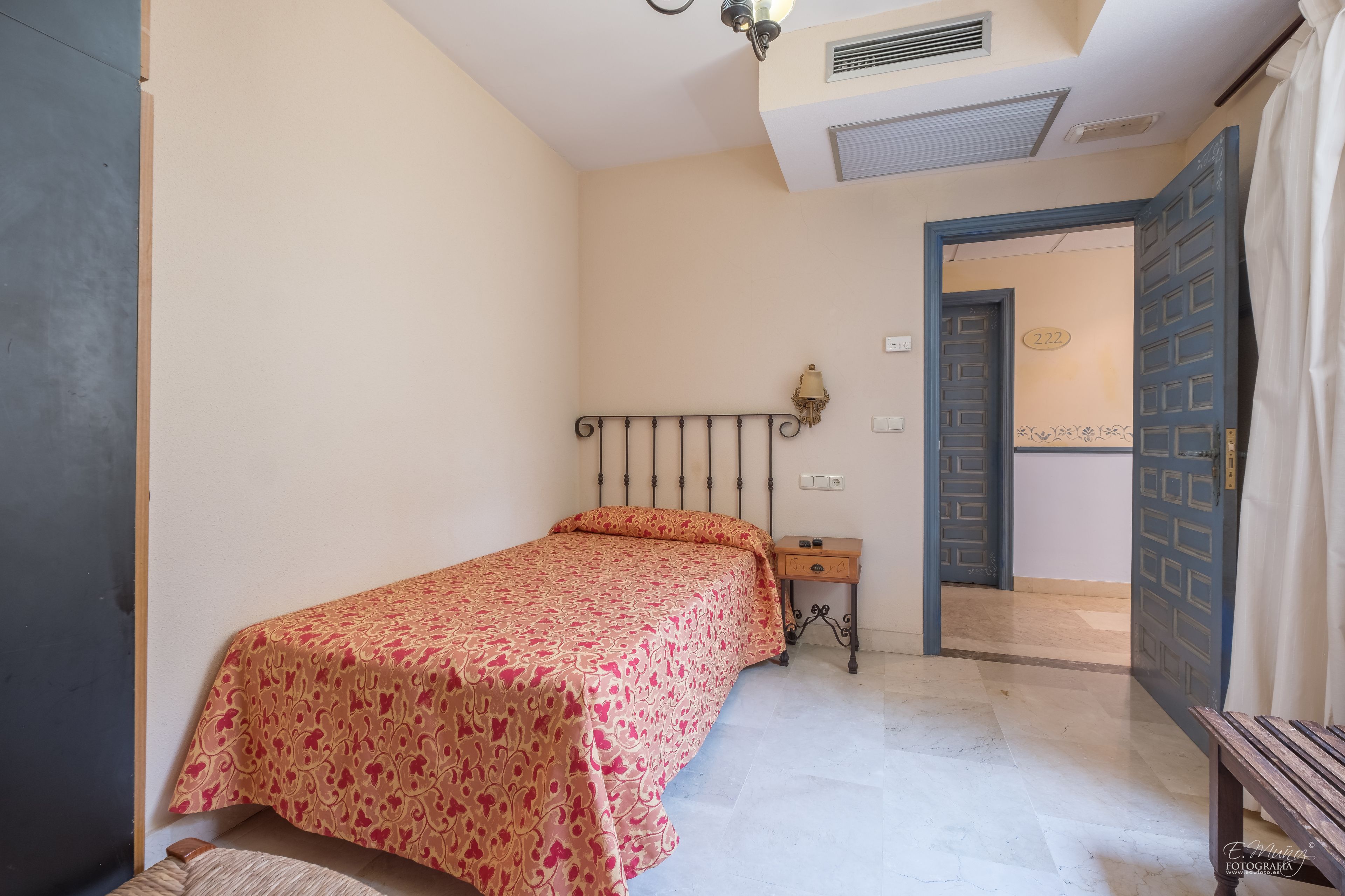 Un dormitorio con cama, mesita de noche y puerta que da a otra habitación.