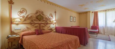 A hotel room with a large bed, a desk, a chair, and a decorative headboard.