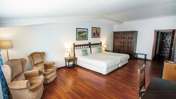 A bedroom with a double bed, two armchairs, a wooden wardrobe, and a desk.