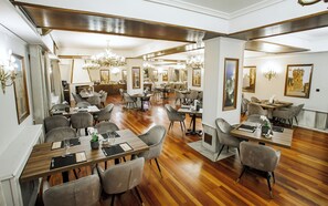 A spacious dining area with multiple tables and chairs, wooden flooring, and chandeliers.