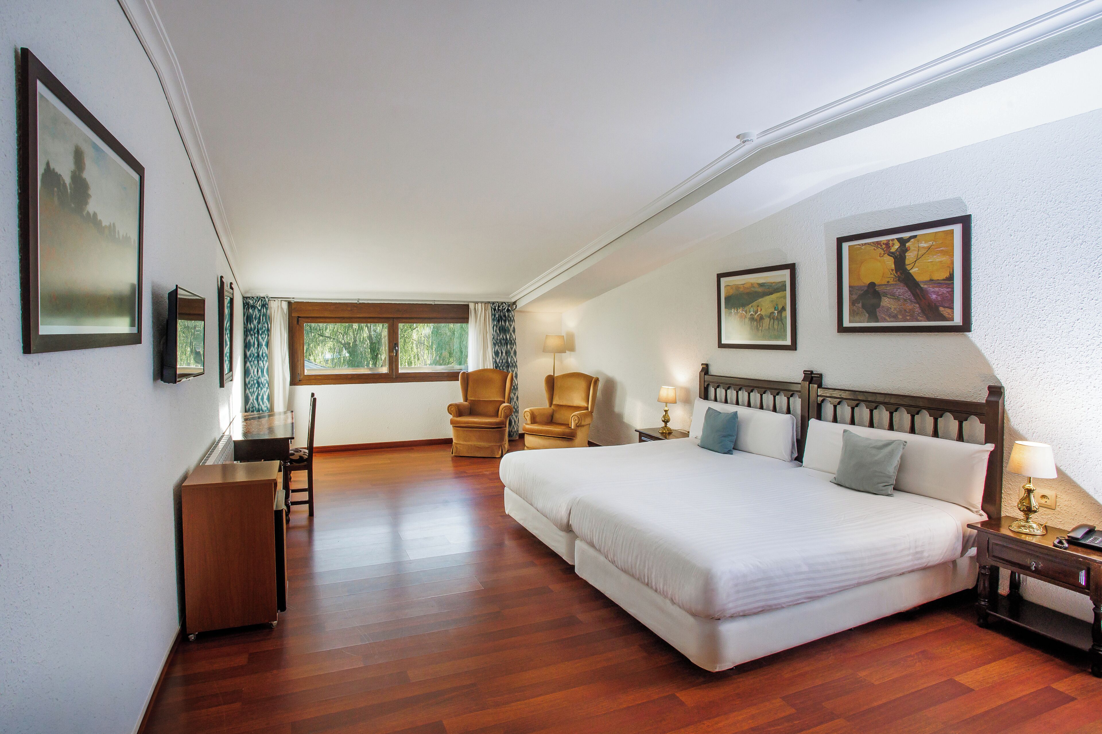 A spacious bedroom with a large bed, two chairs, a desk, and a window with curtains.