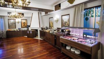 Une chambre d’hôtel avec un plancher en bois, un buffet proposant divers plats, un lustre et des tableaux encadrés accrochés aux murs.