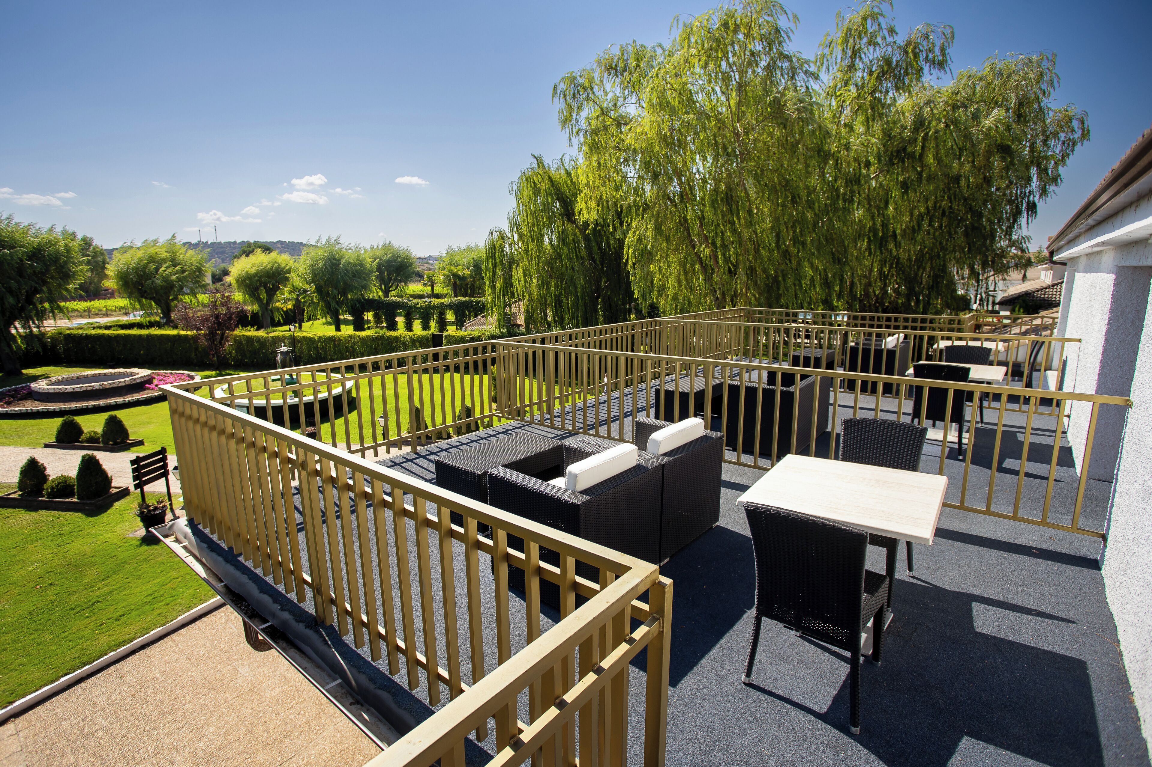 Un patio en la azotea con muebles de exterior, vistas a un jardín ajardinado y cielo despejado.