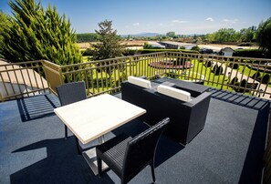 An outdoor patio with a table and chairs, a view of a landscaped garden, and a distant view of a body of water and mountains.