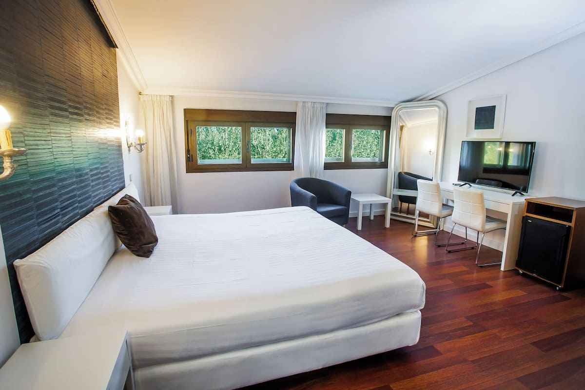 Una habitació d'hotel amb un llit gran, una taula, una cadira, una televisió i finestres amb cortines.