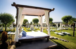 Una cama con dosel en un jardín con sillones y sombrillas.