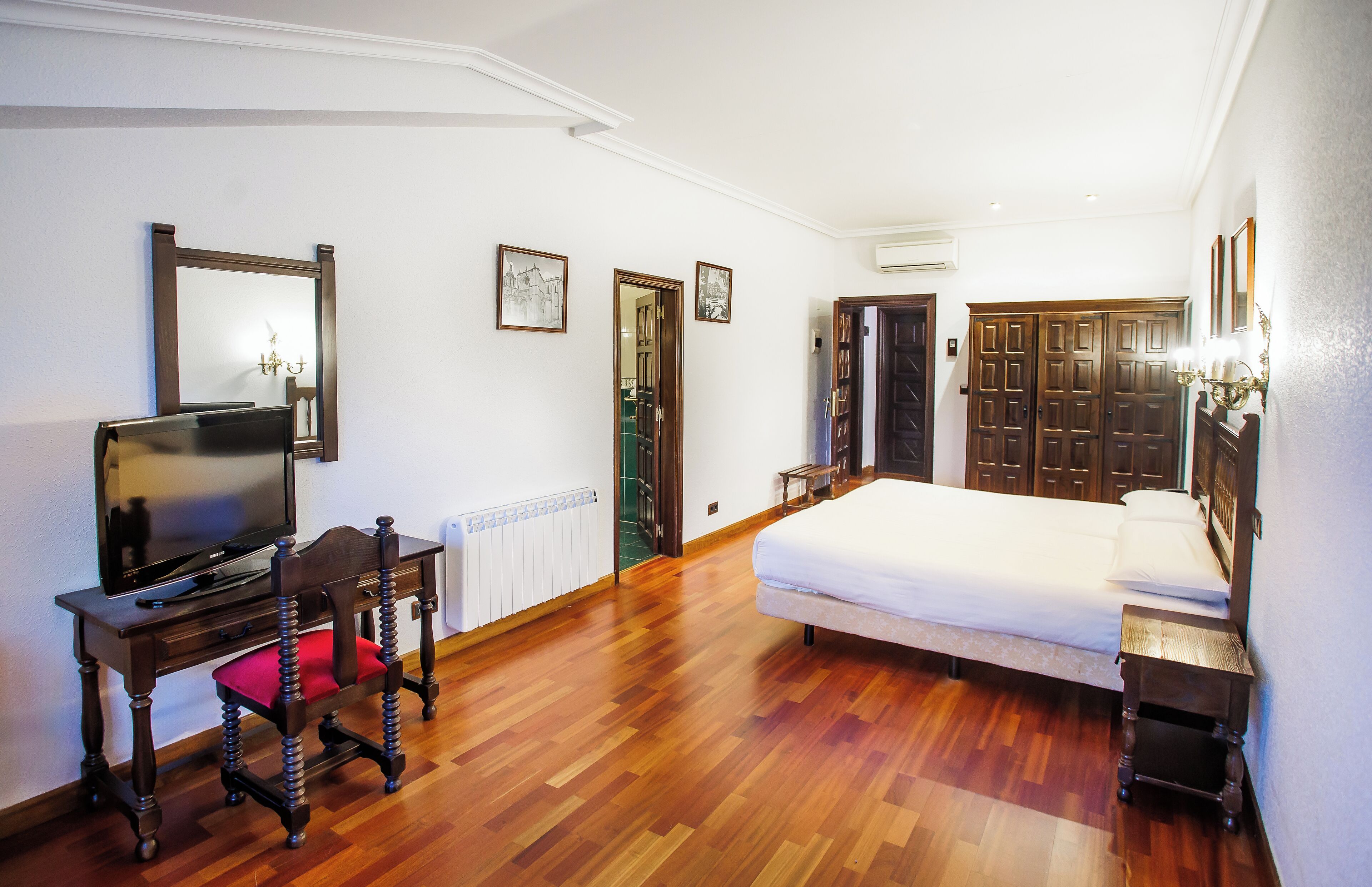 Un dormitorio con una cama, televisión sobre una mesa de madera, una silla y un armario.